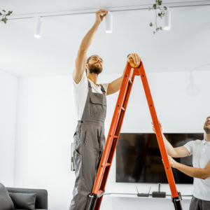 Two repairmen or professional electricians installing light spots, standing on the ladder in the living room of the modern apartment